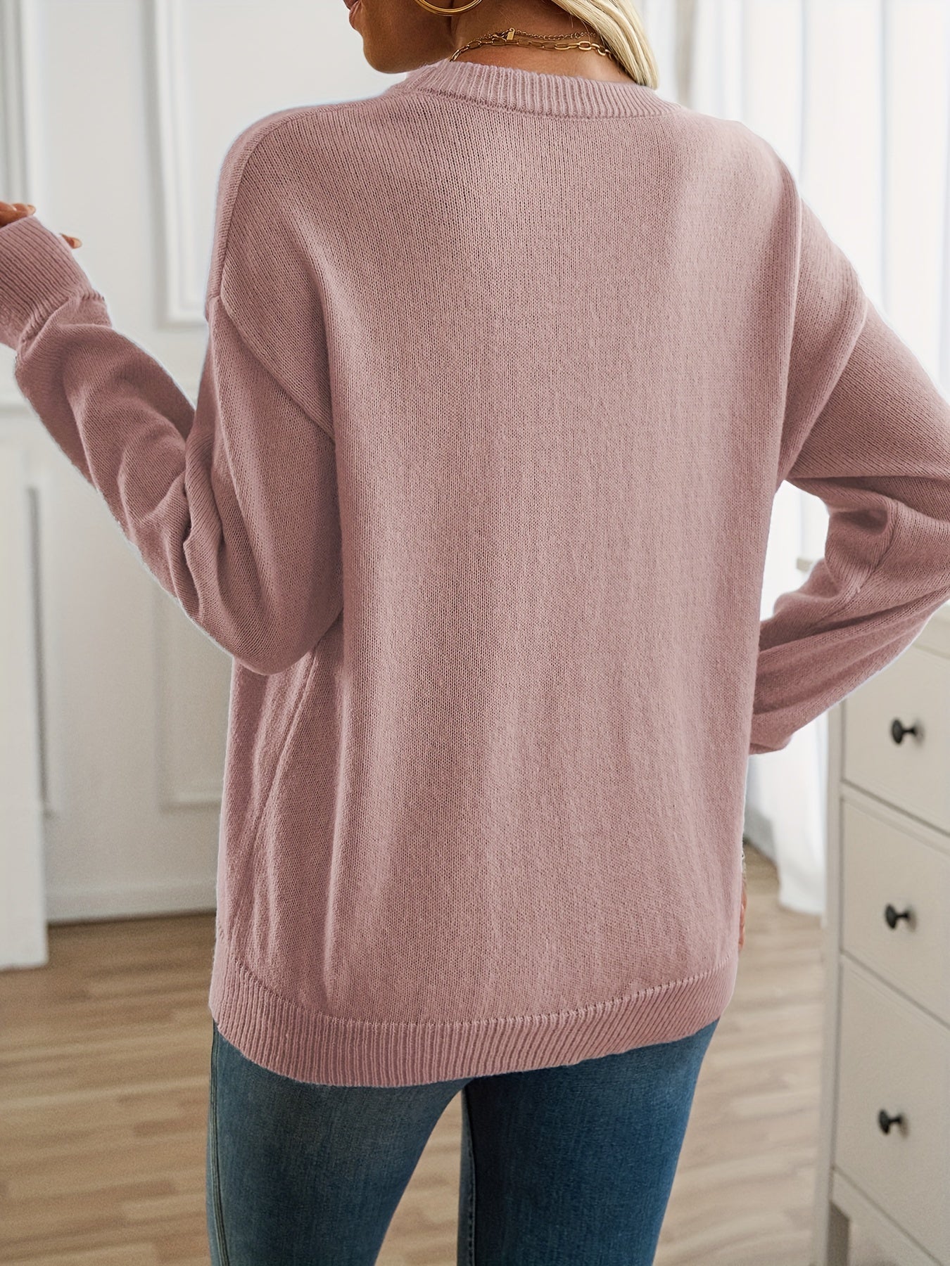 Person wearing a pink sweater in a room with white walls and furniture.