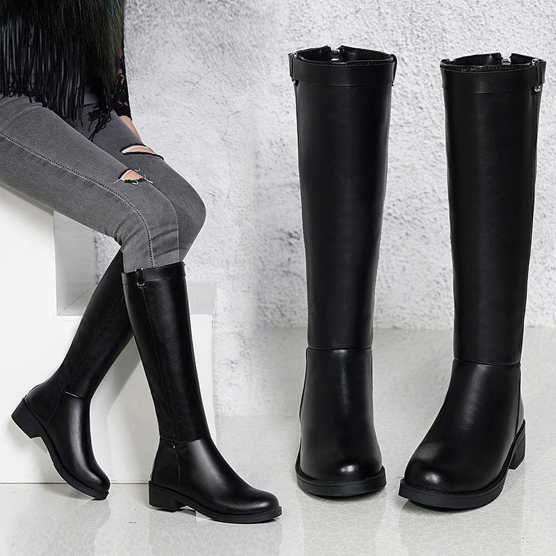 Black knee-high boots displayed on a light gray surface with a neutral background.