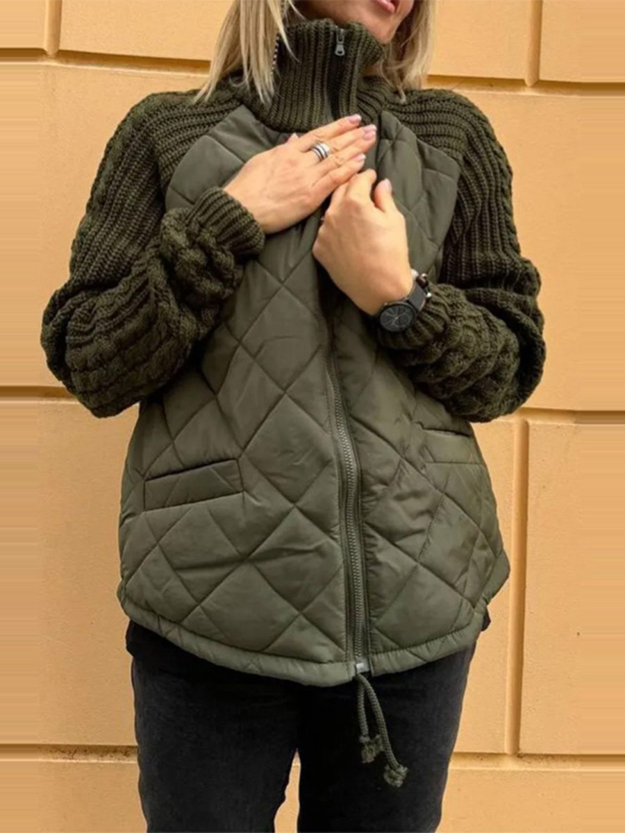 Person wearing a green quilted vest over a dark sweater against a beige wall.