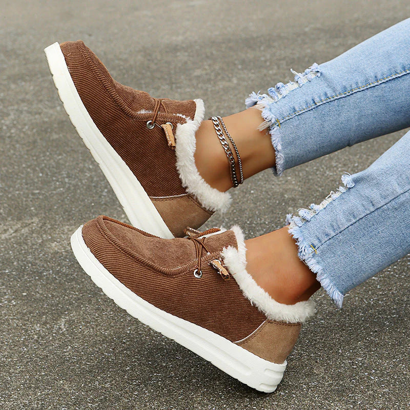 Brown sneakers with white fur lining worn with light blue jeans on a concrete surface.