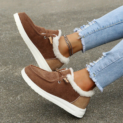 Brown sneakers with white fur lining worn with light blue jeans on a concrete surface.