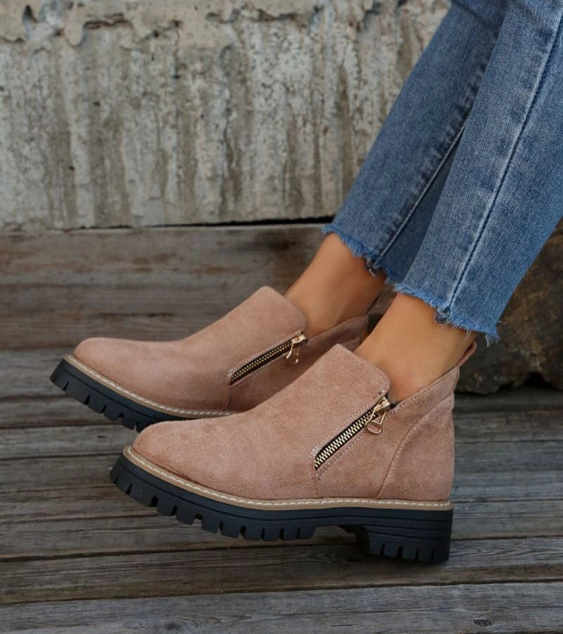 Tan suede boots with zippers worn by a person on wooden steps.