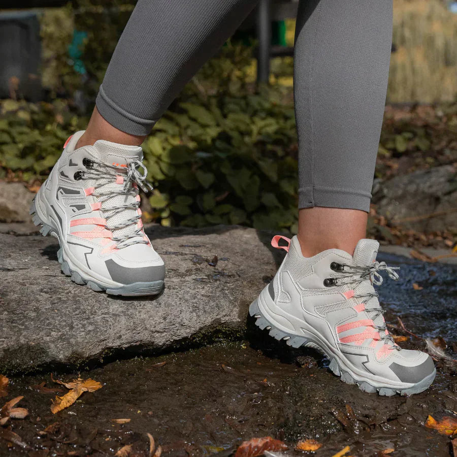 Person wearing gray hiking boots with pink accents on a stone path.