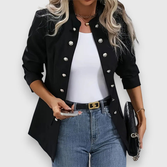 Person wearing a black jacket with silver buttons, white top, blue jeans, and holding a phone and black clutch.