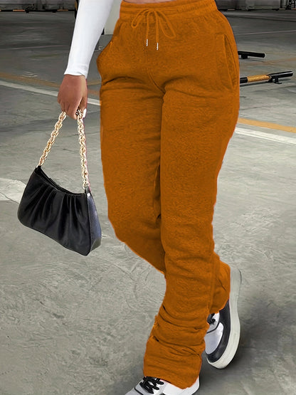 Person wearing mustard yellow jogger pants holding a black handbag on a concrete surface.