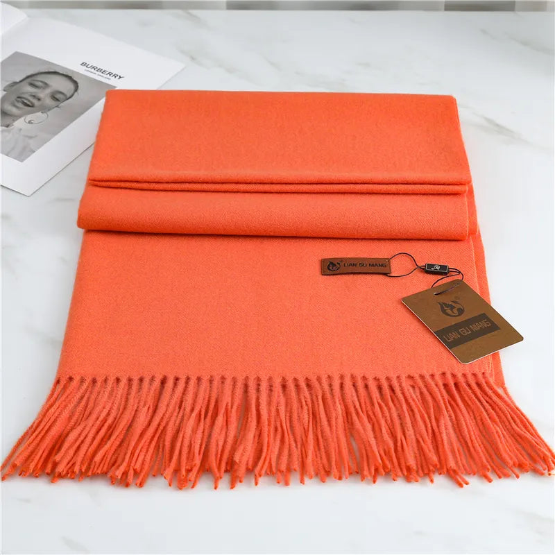 Orange scarf with fringes and a tag on a white surface