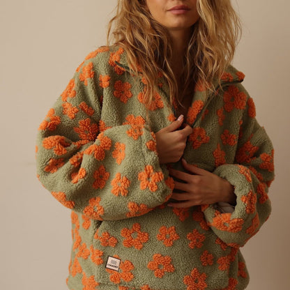 Person wearing a green fleece jacket with orange floral patterns on a beige background