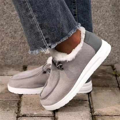 Gray winter boots with white soles worn with blue jeans on a stone surface.