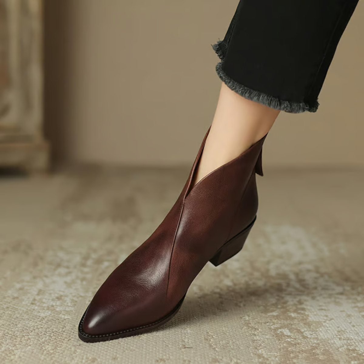 Brown leather ankle boot worn with black pants on a neutral background