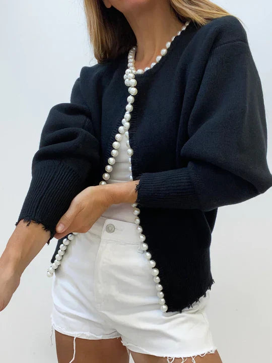 Person wearing a navy cardigan with pearl trim on a white background
