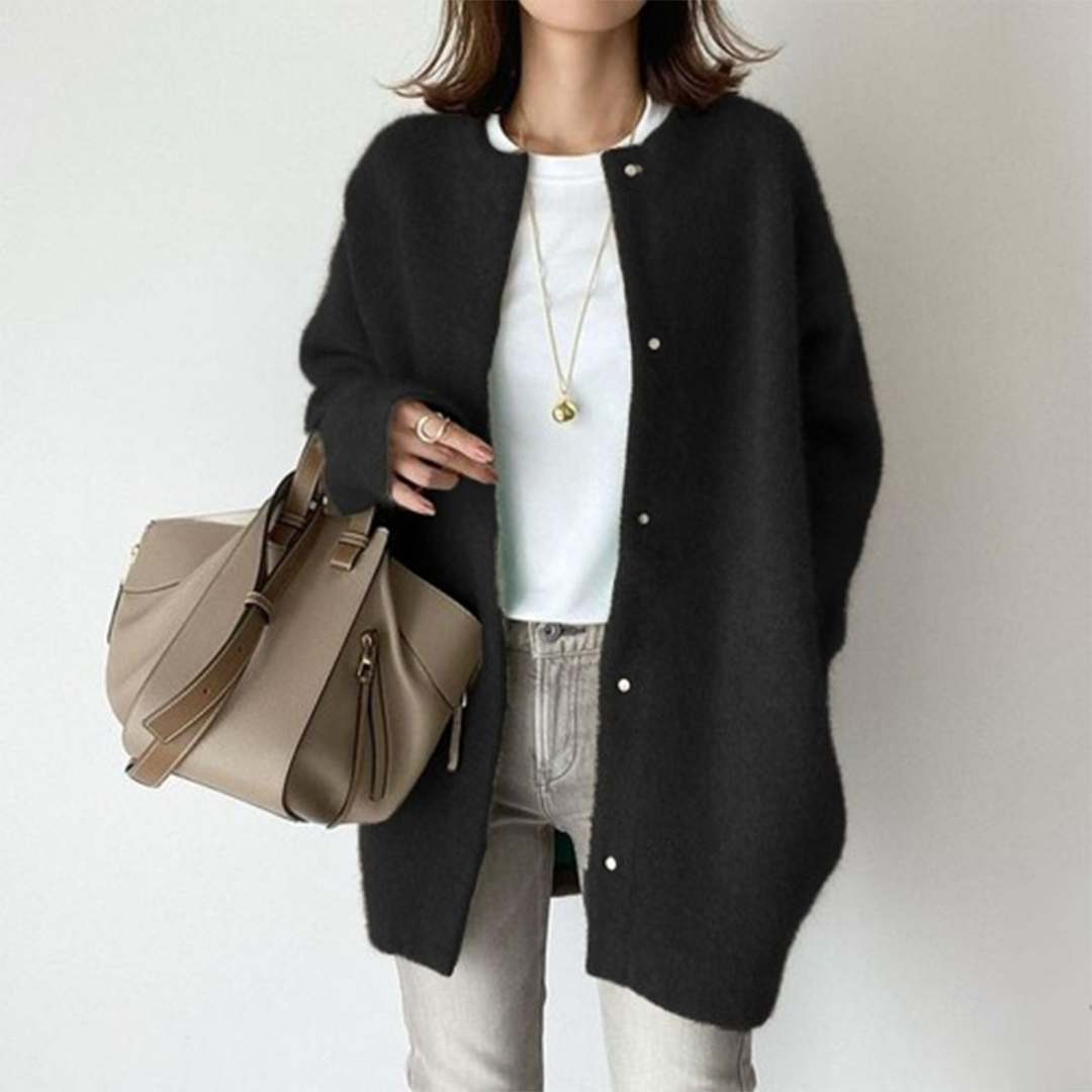Person wearing a black cardigan, white shirt, and beige pants holding a beige handbag on a plain background