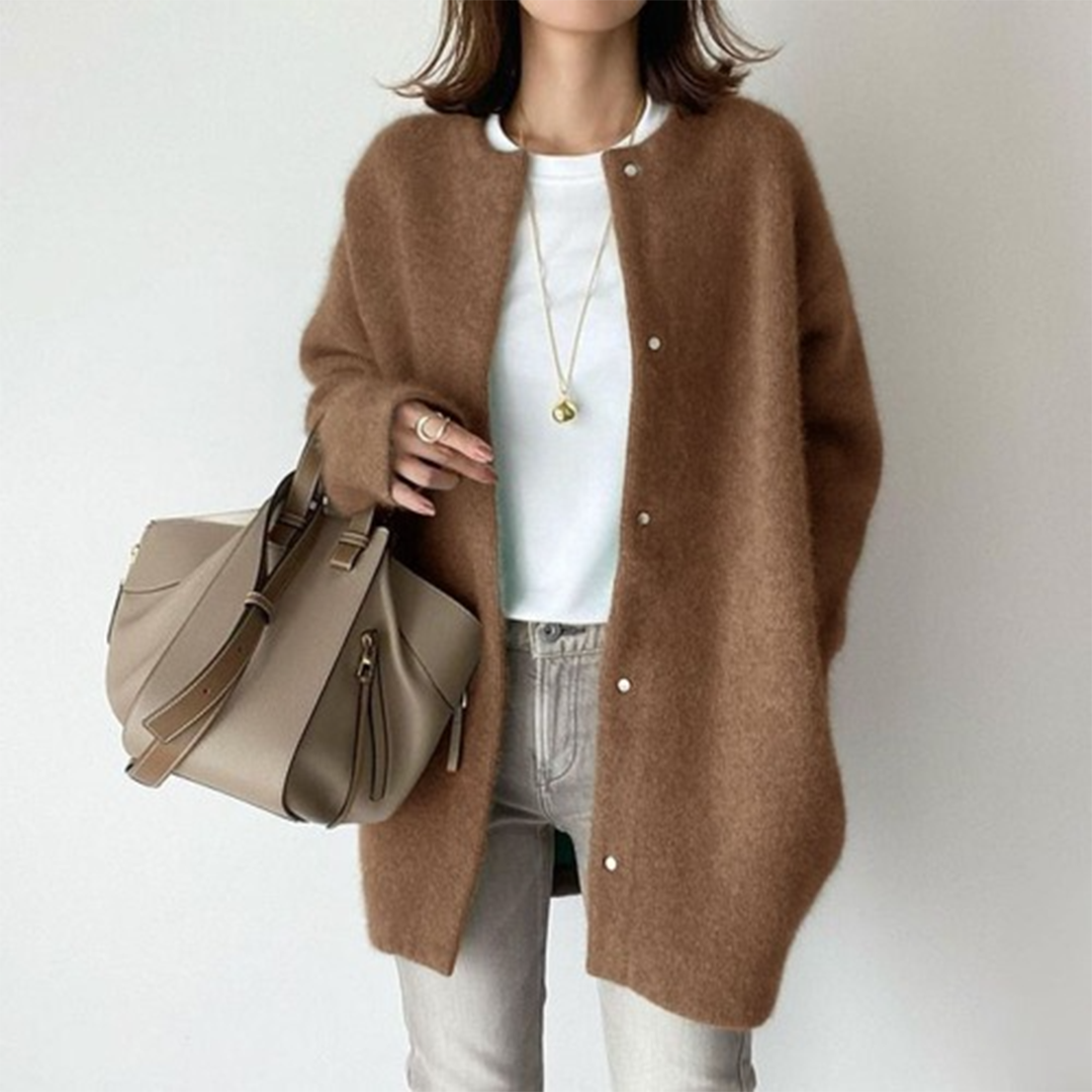 Person wearing a brown cardigan holding a beige handbag against a plain background
