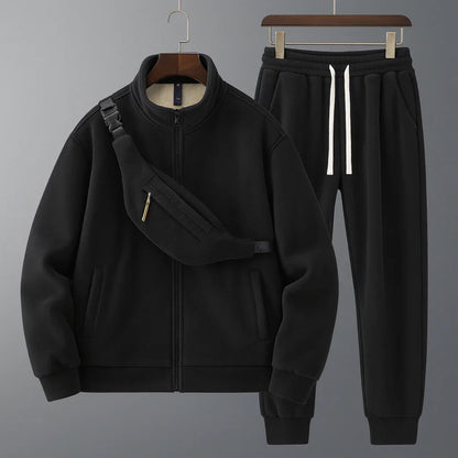 Black tracksuit with jacket and pants on hangers against a gray background
