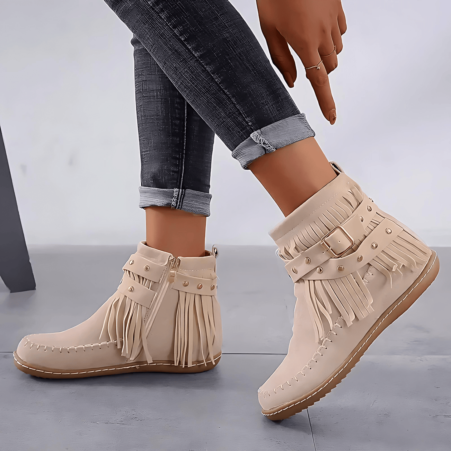 Beige fringe boots worn with rolled-up jeans on a gray background