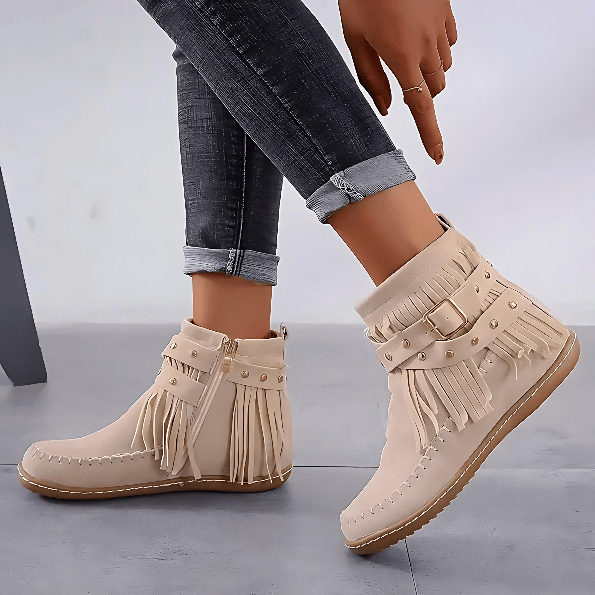 Beige fringe boots worn with rolled-up jeans on a gray background