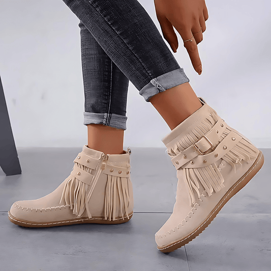 Beige fringe boots worn with rolled-up jeans on a gray background