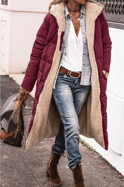Person wearing a long burgundy puffer coat with beige lining, blue jeans, and brown boots on a street.