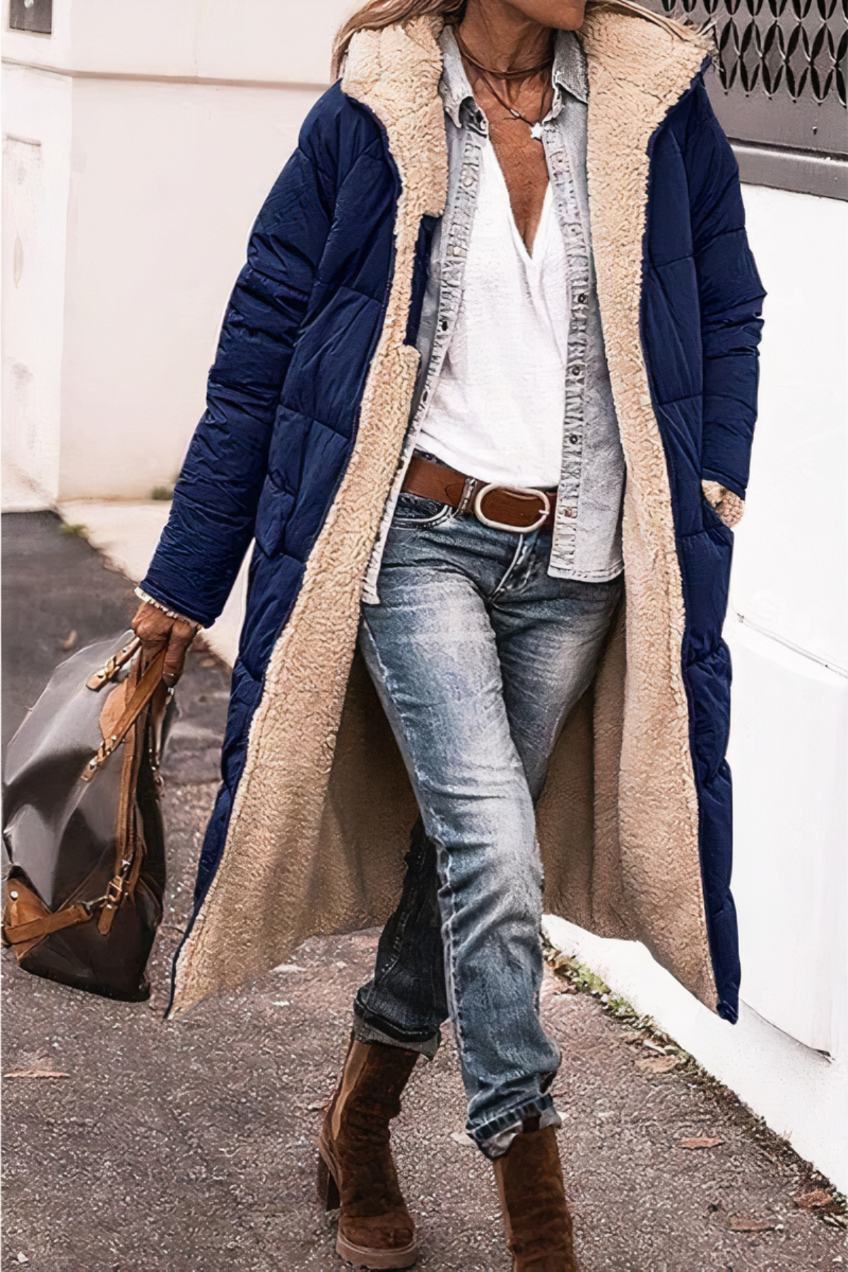 Person wearing a long navy coat with beige fur lining, blue jeans, and brown boots.