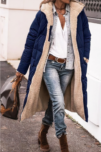 Person wearing a long navy coat with beige fur lining, blue jeans, and brown boots.