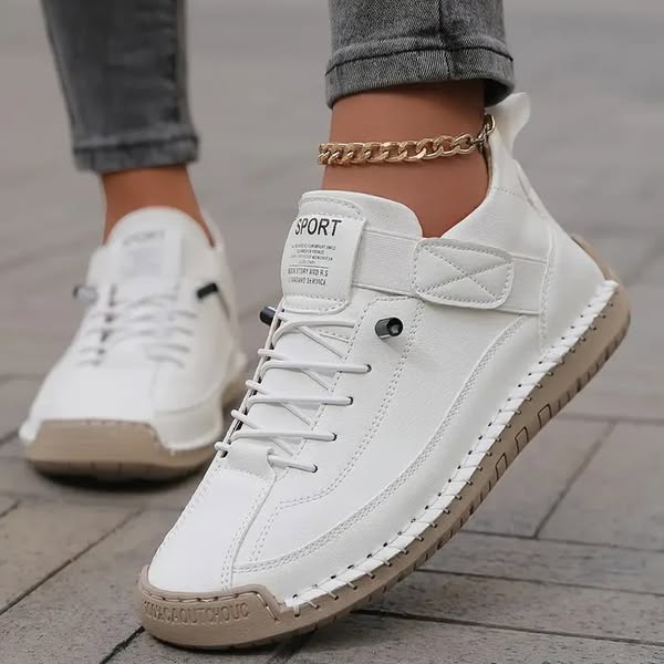 White sneakers with beige soles worn on a pavement surface