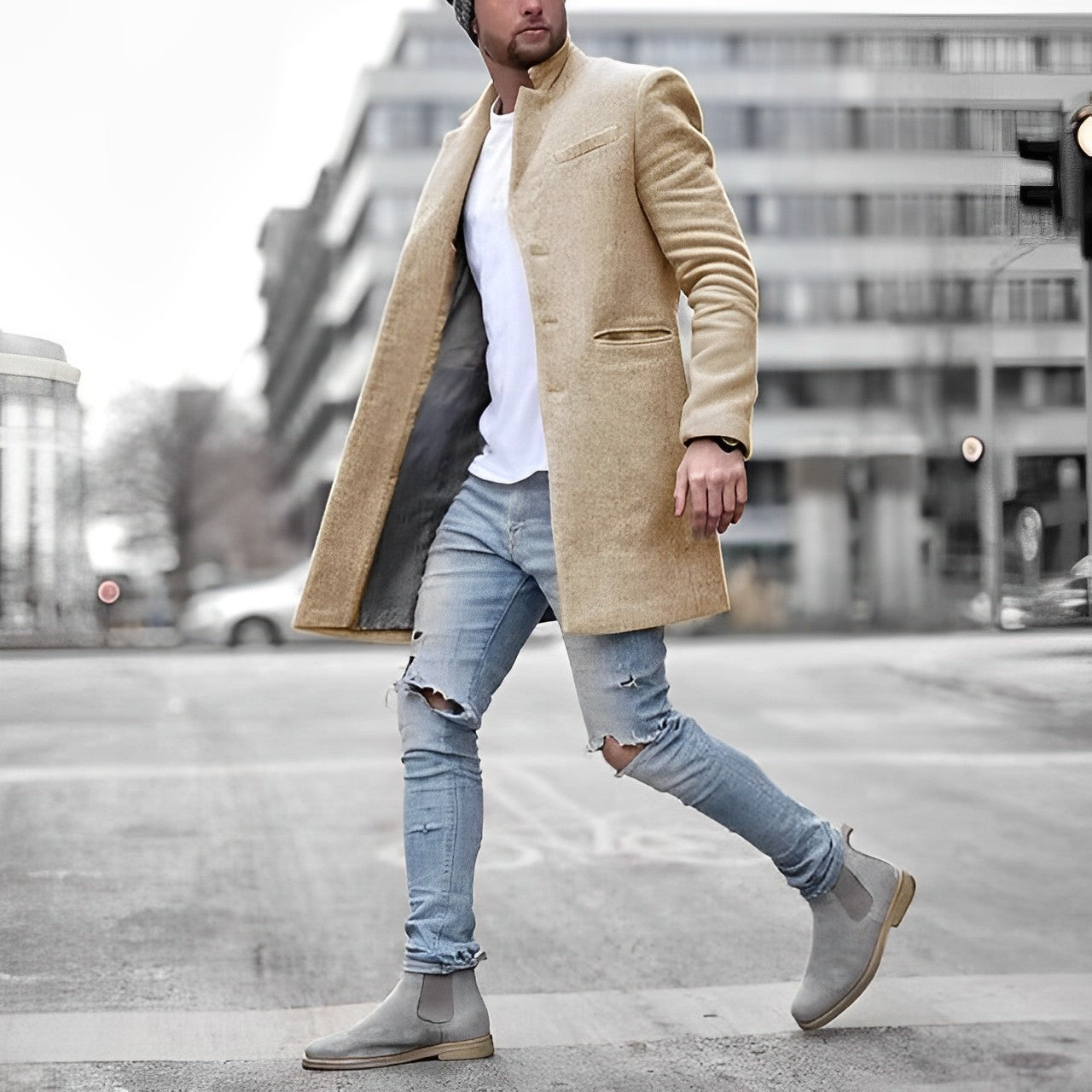 Man wearing a beige coat, white shirt, ripped jeans, and gray boots walking on a city street.