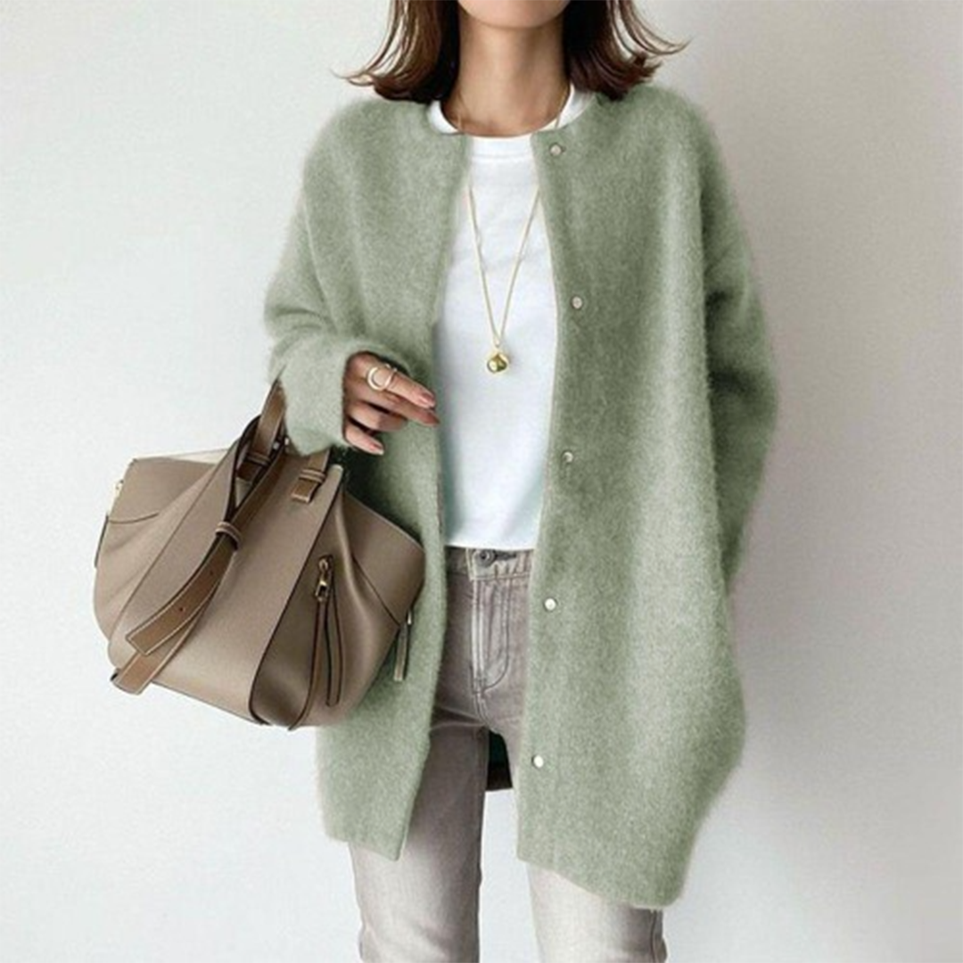 Person wearing a green cardigan holding a beige handbag on a plain background