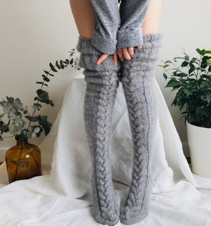 Person wearing gray knitted leg warmers with a white curtain and plants in the background