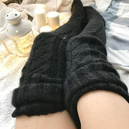 Black cable knit socks worn on a person's feet with a cozy background.