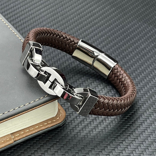 Brown braided leather bracelet with silver clasp on a textured surface