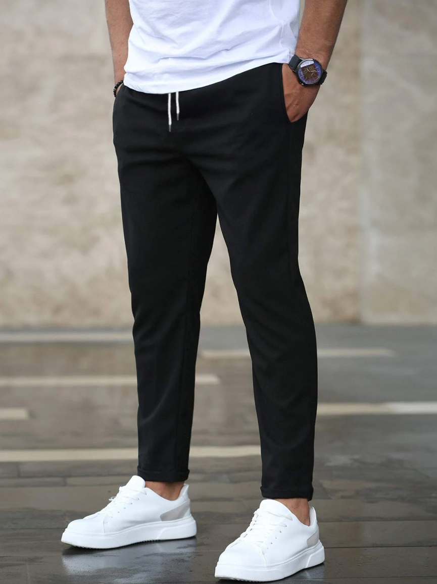 Person wearing black pants and white sneakers against a neutral background
