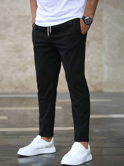 Person wearing black pants and white sneakers against a neutral background