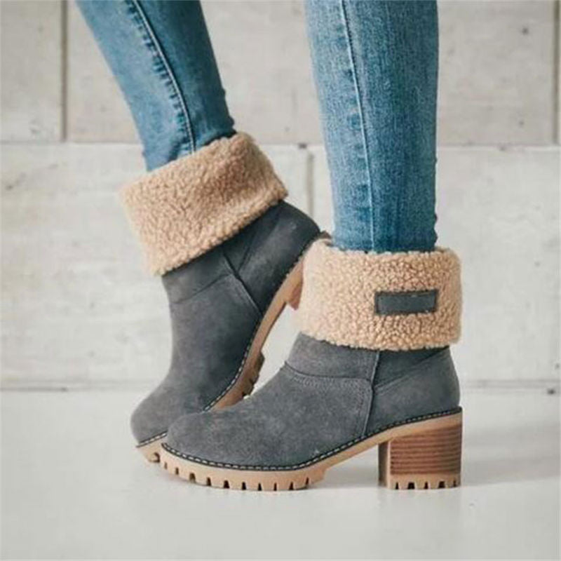 Gray ankle boots with beige fur trim worn with blue jeans on a light wooden floor.