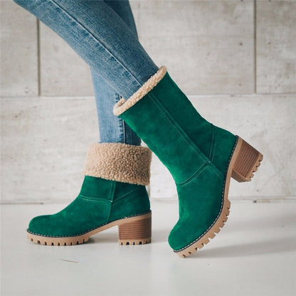Green suede boots with beige fur lining worn with blue jeans on a light wooden floor.