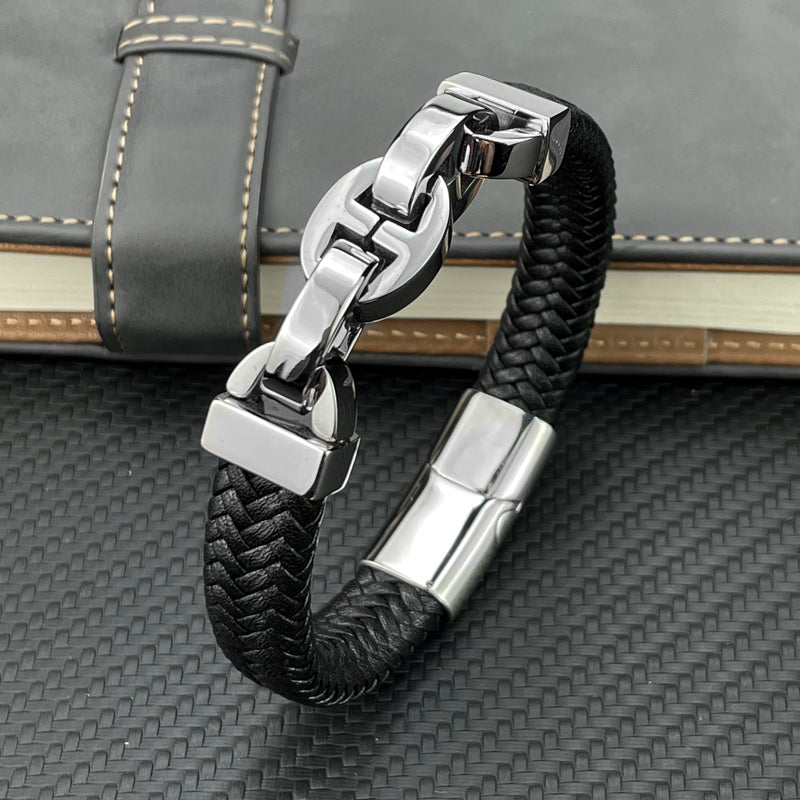 Black braided leather bracelet with silver clasp on a textured surface