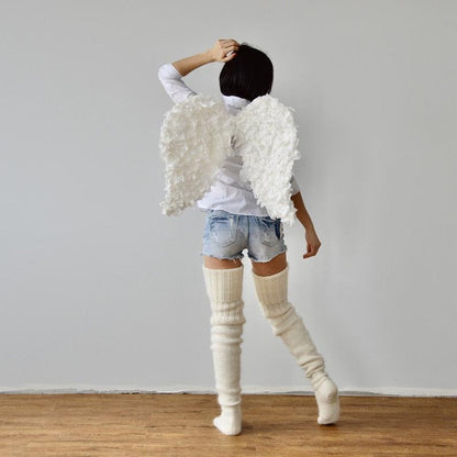 Person wearing angel wings and knee-high socks standing against a plain wall.