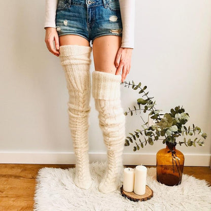 Person wearing white knee-high socks with denim shorts and a vase with greenery on a rug.