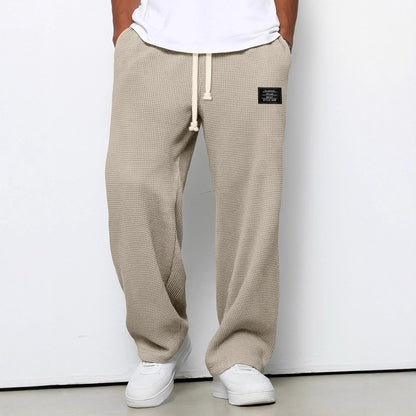 Beige waffle-textured pants with a brand logo worn by a person on a white background