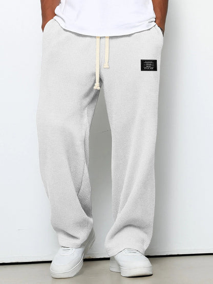 Person wearing light gray textured sweatpants with a brand logo on a white background