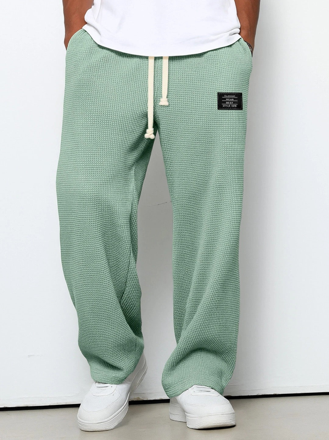 Person wearing green textured sweatpants with a white label on a plain background