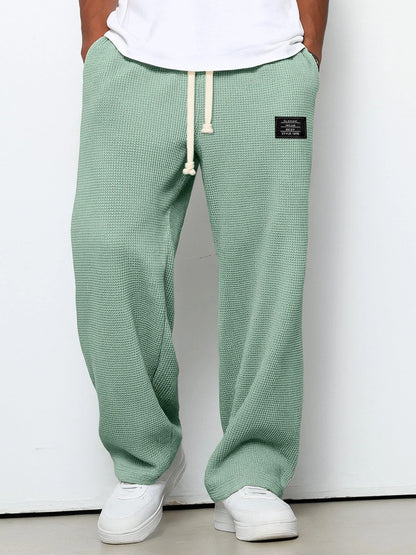 Person wearing green textured sweatpants with a white label on a plain background