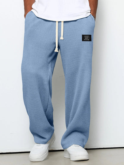 Person wearing blue textured sweatpants with a white label on a plain background