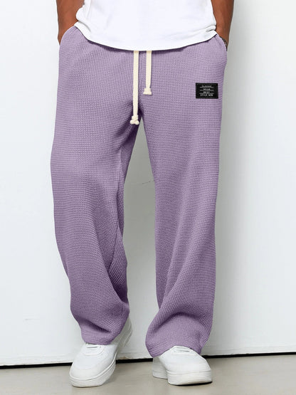 Person wearing purple textured sweatpants with a white label on a plain background