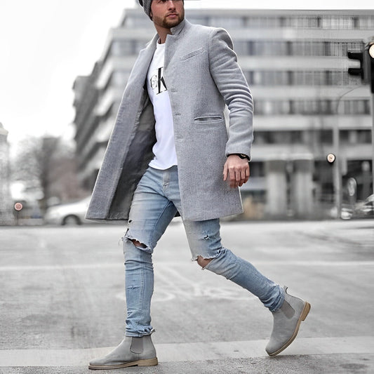 Man walking on a street wearing a gray coat, white t-shirt, ripped jeans, and gray boots.