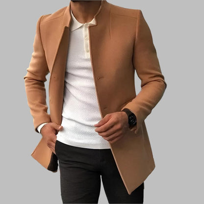Person wearing a tan coat over a white shirt and black pants on a gray background