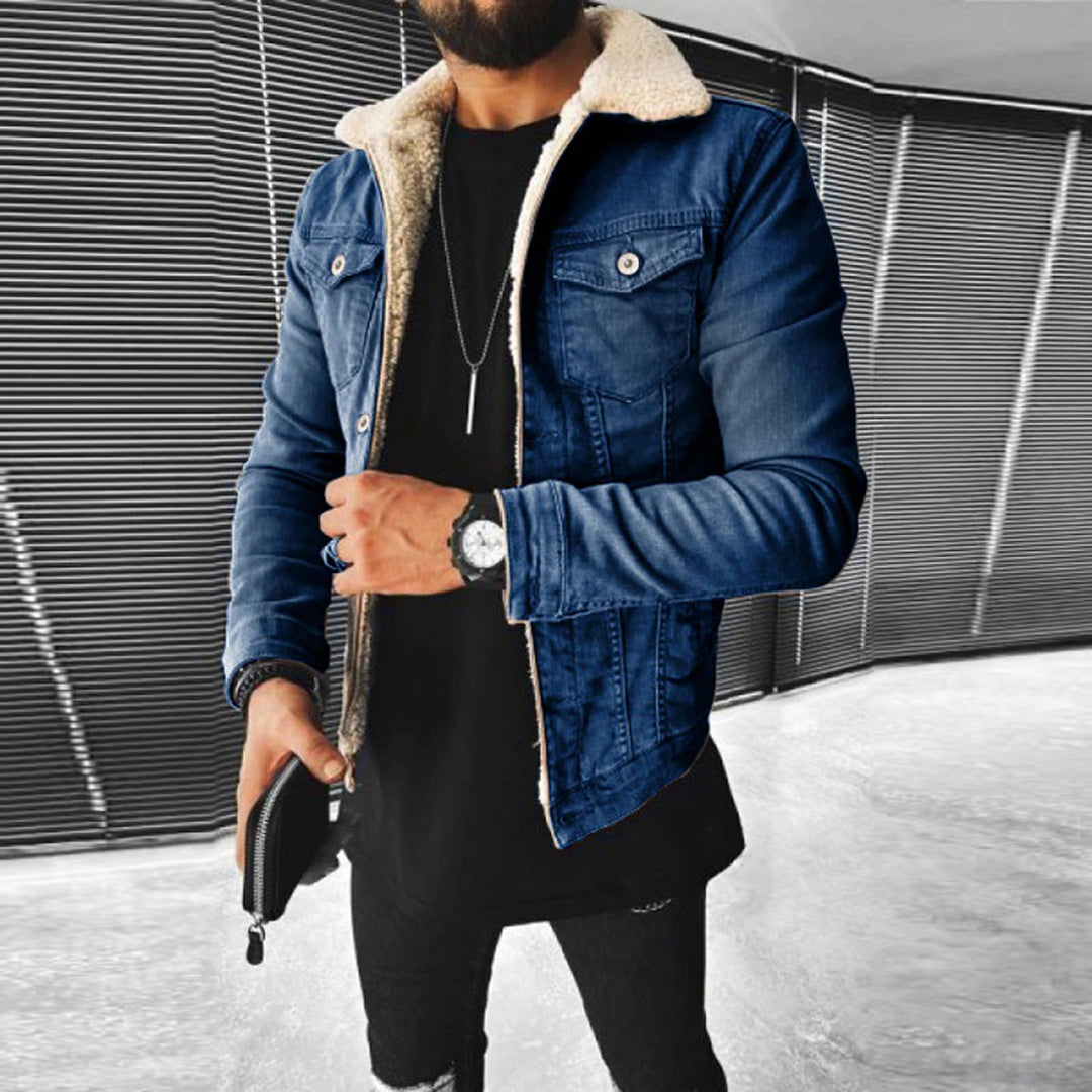 Man wearing a blue denim jacket with shearling collar and black pants against a modern interior background.
