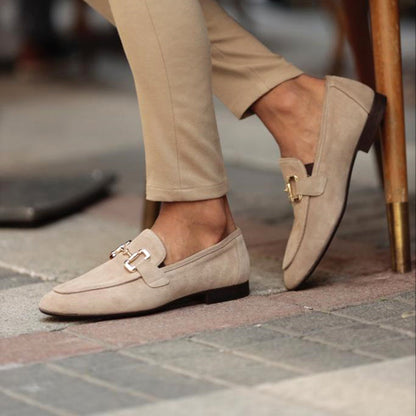 Beige loafers worn with beige pants on a pavement.