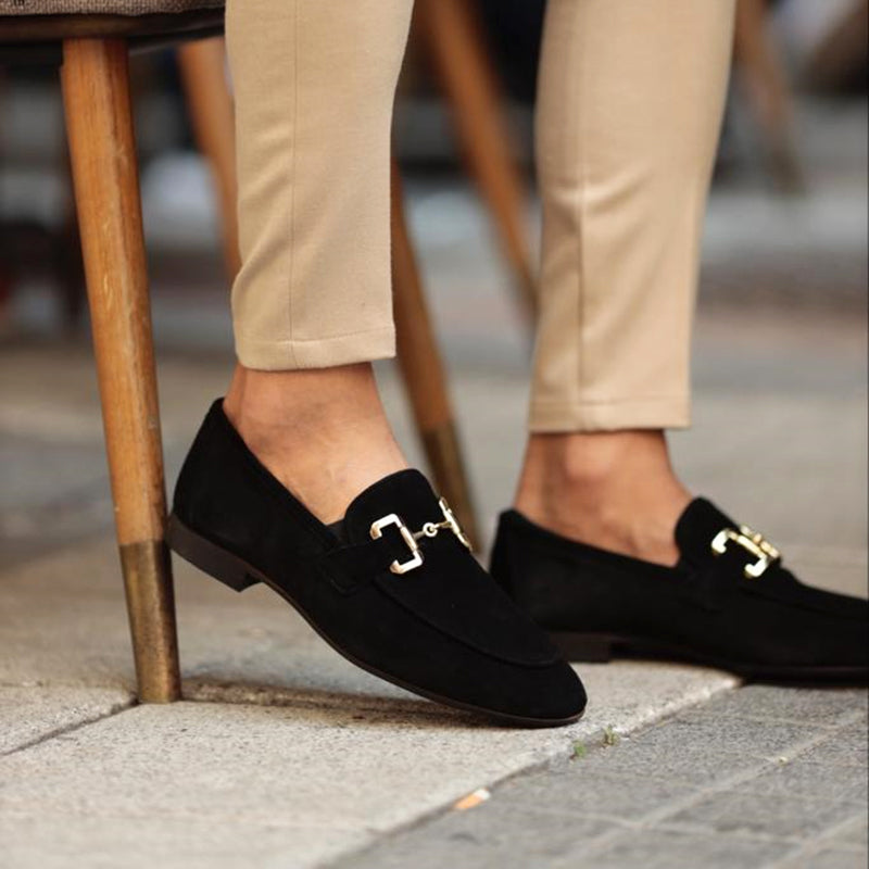 Black loafers with gold buckles worn by a person on a sidewalk.