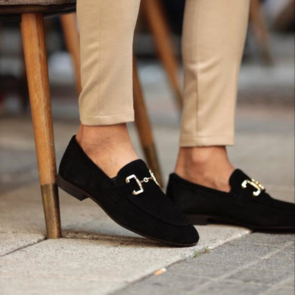 Black loafers with gold buckles worn by a person on a sidewalk.