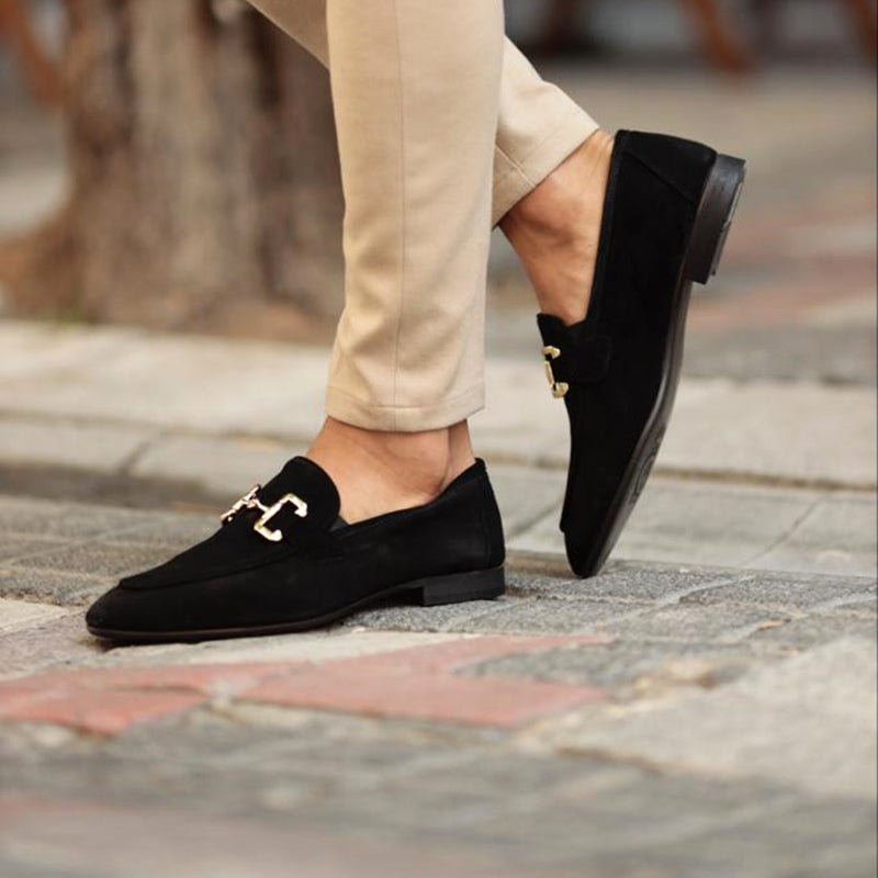 Black loafers with gold buckles worn on a stone pavement.