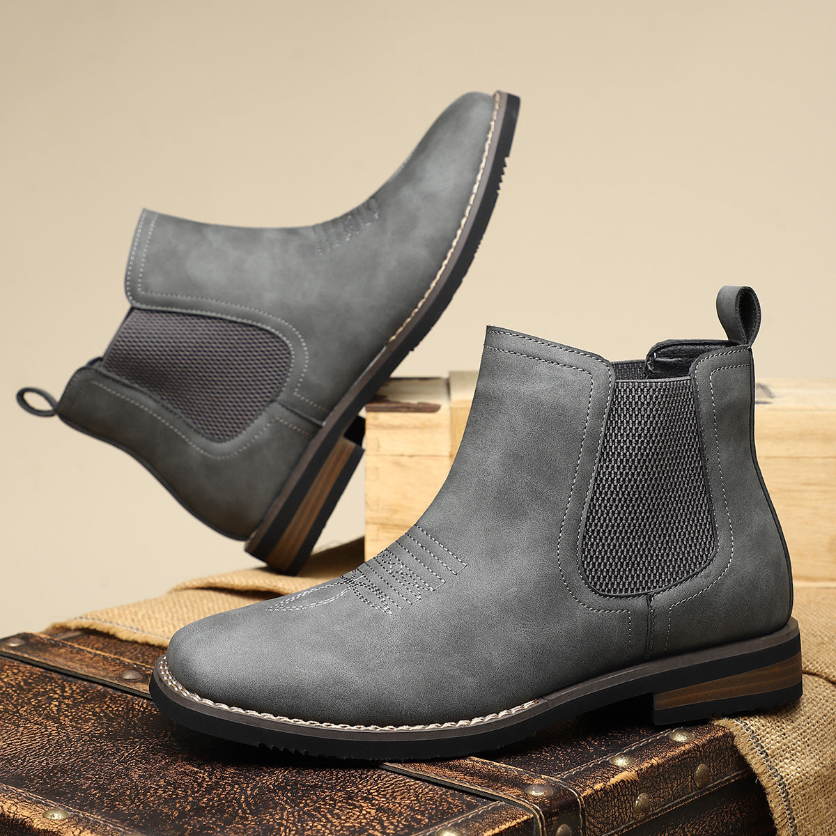 Gray Chelsea boots on a wooden surface with a beige background